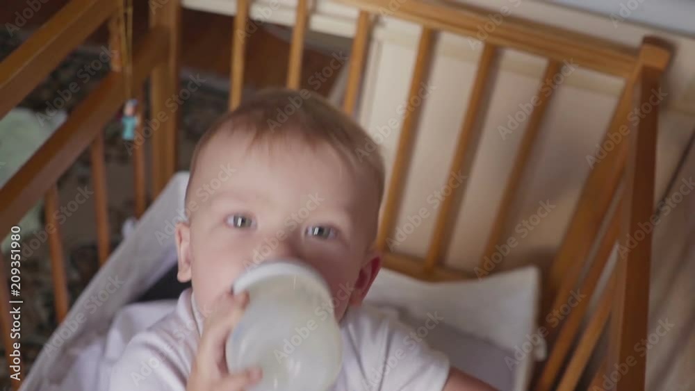 Two year old boy drinking milk from plastic bottle in his bed looking up Two year old boy drinking milk from plastic bottle in his bed looking up