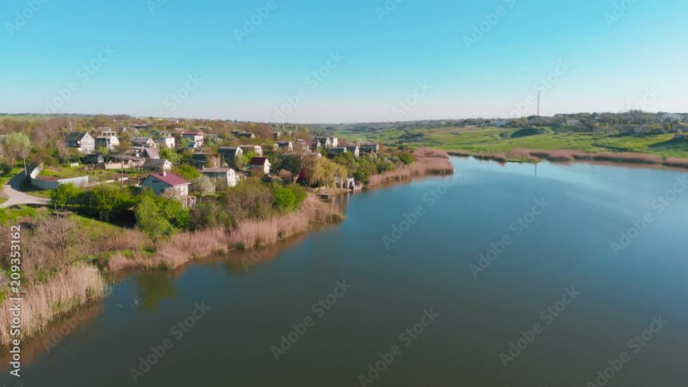 The flight of drones over country houses in the hills on the shore of the pond early in the morning at dawn. Flight over the water at a bird's eye view. Aerial view 4K The flight of drones over country houses in the hills on the shore of the pond early in the morning at dawn. Flight over the water at a bird's eye view. Aerial view 4K