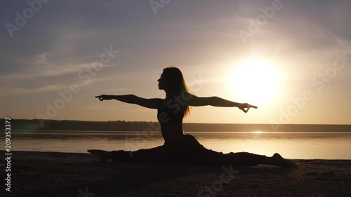 Beautiful woman's silhouette doing yoga, split on sea coast. Morning sunrise, smog sun on thee backstage photo