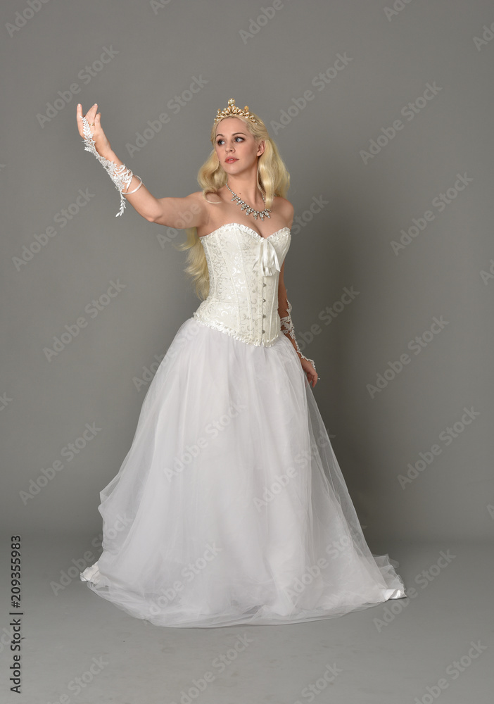 Fototapeta premium full length portrait of blonde girl wearing white corset gown. standing pose on grey studio background.