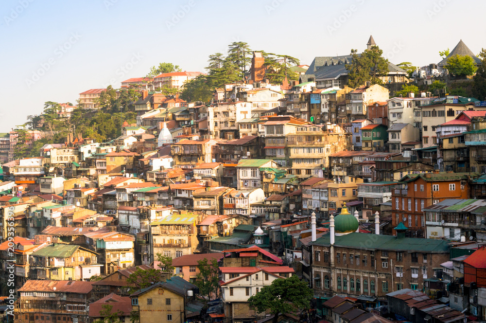 Colorful buildings on the side of a mountainside on a dawn morning. Shot in shimla it shows the sloping roof buildings with trees in between