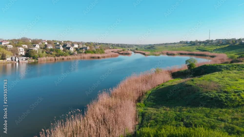 The flight of drones over country houses in the hills on the shore of the pond early in the morning at dawn. Flight over the water at a bird's eye view. Aerial view 4K The flight of drones over country houses in the hills on the shore of the pond early in the morning at dawn. Flight over the water at a bird's eye view. Aerial view 4K