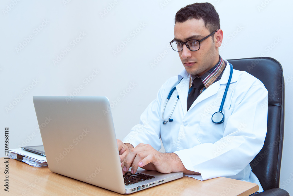 Doctor sitting at the desk, using laptop typing and searching data from the internet or searching patient record data. Doctor sitting at the desk, using laptop typing and searching data from the internet or searching patient record data.