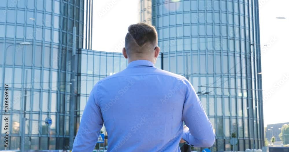 Young handsome businessman in blue shirt walking along the street, skyscraper background.