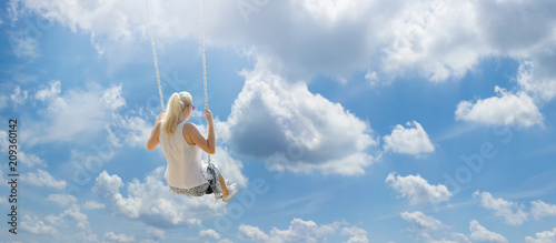 Blonde girl with ponytail flying high among the white clouds on a swing