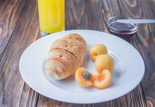 breakfast - a croissant, apricots and juice, on a wooden background