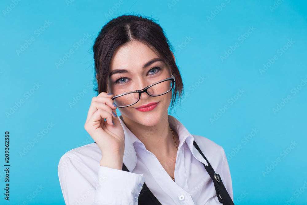 Pretty young smiling brunette woman in glasses and waistcoat looking at camera on blue background. Pretty young smiling brunette woman in glasses and waistcoat looking at camera on blue background.