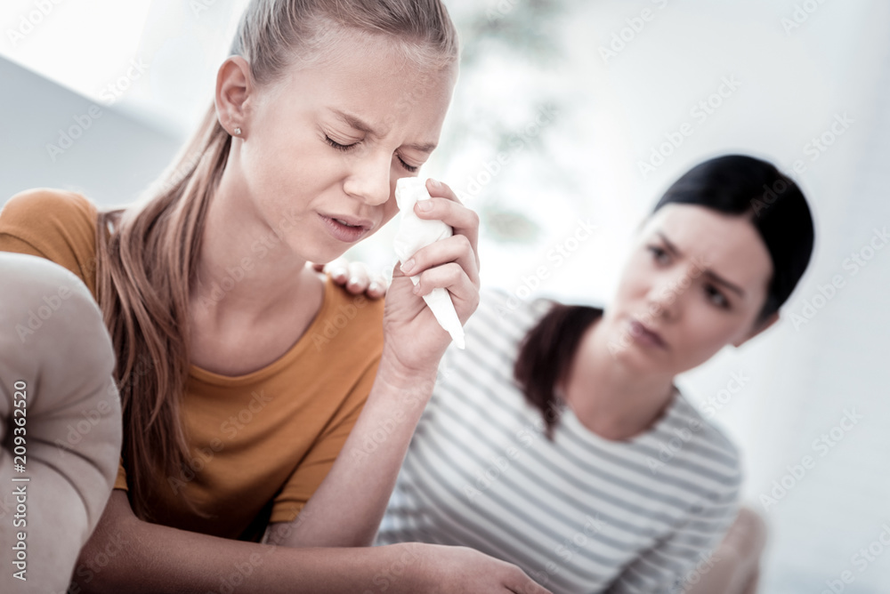 Super girls never cry. Close up of light haired girl crying and using a napkin while her mother supporting her