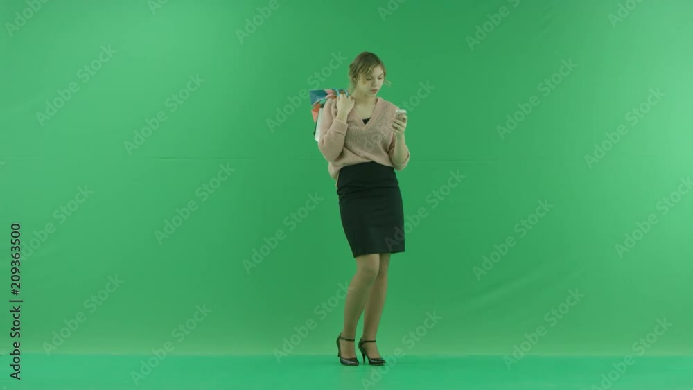 Pretty shopping woman is surfing the internet with shopping bags. Female shopper holding shopping bags sideways on green background in studio. Pretty shopping woman is surfing the internet with shopping bags. Female shopper holding shopping bags sideways on green background in studio.