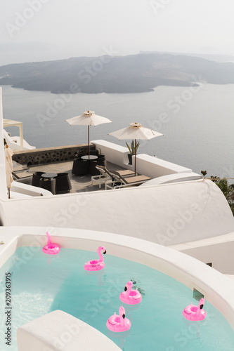 Pink toy flamingo swimming in a pool in luxury vila on Santorini island overlooking the volcano caldera  Greece