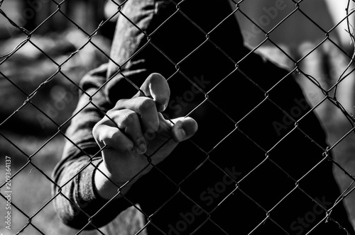 Young unidentifiable teenage boy holding the wired garden at the correctional institute in black and white, conceptual image of juvenile delinquency, focus on the boys hand. photo