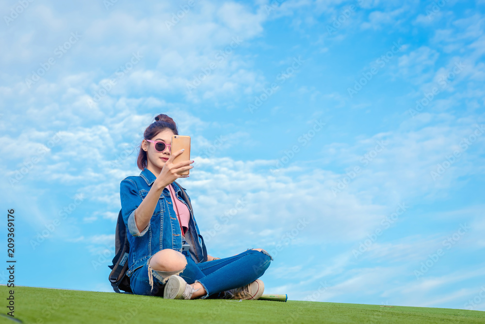 Asain woman take a picture of herself with a smartphone on blue sky and white clouds background. Asain woman take a picture of herself with a smartphone on blue sky and white clouds background.