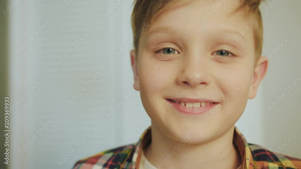 Portrait of the cute blonde boy in the plaid shirt looking at the camera and smiling sincerely. White wall background. Close up. Indoors Portrait of the cute blonde boy in the plaid shirt looking at the camera and smiling sincerely. White wall background. Close up. Indoors