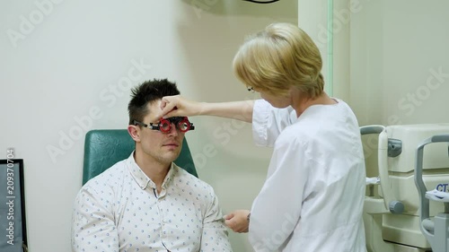 Female Optometrist Doing Sight Testing For Patient In Hospital with phoropter, optometrist trial frame, visual inspection device. checks vision in doctor's office photo