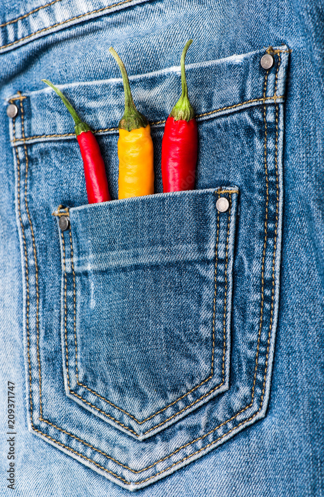 Pocket of jeans staffed with red and yellow chilly peppers, denim  background. Piquant secret in pocket of pants, top view. Peppers in back  pocket of blue jeans. Hot sensations concept Stock Photo