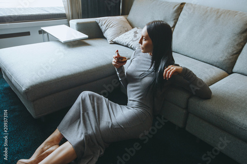 Luxurious young brunette sitting on floor in living room with glass of whiskey