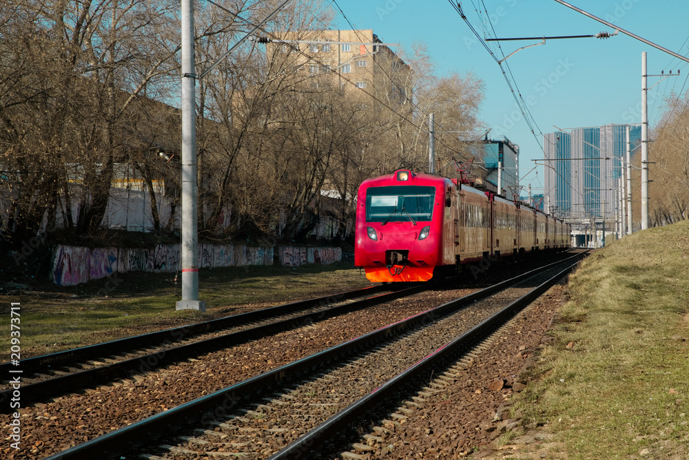 Red train moves in a city in bright sunny day. Developed transport network of large city. Front view.