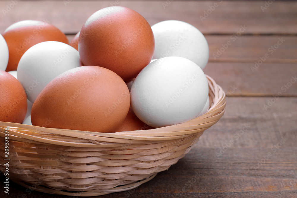 Brown and white chicken eggs in a wicker basket on a brown wooden background. Brown and white chicken eggs in a wicker basket on a brown wooden background.