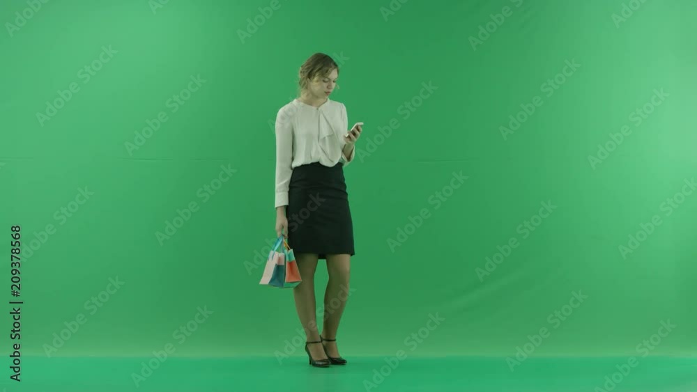 Pretty shopping woman is surfing the internet with shopping bags. Female shopper holding shopping bags front on green background in studio. Pretty shopping woman is surfing the internet with shopping bags. Female shopper holding shopping bags front on green background in studio.