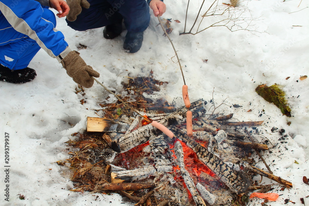 Obraz premium People roast sausages at the stake in nature in the forest. Picnic in nature. Russia, January, 2018.