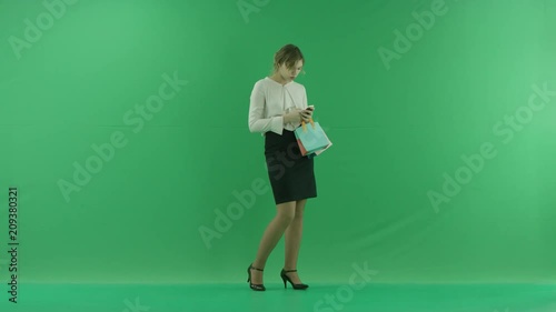 Pretty shopping woman is surfing the internet with shopping bags. Female shopper holding shopping bags front on green background in studio. photo