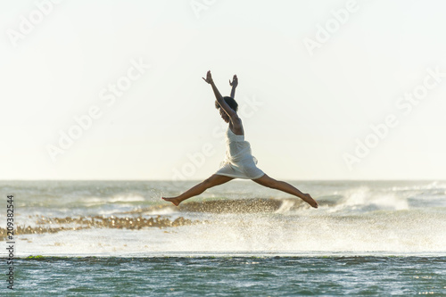 A beautiful young black woman leaps through the air as waves crash around her