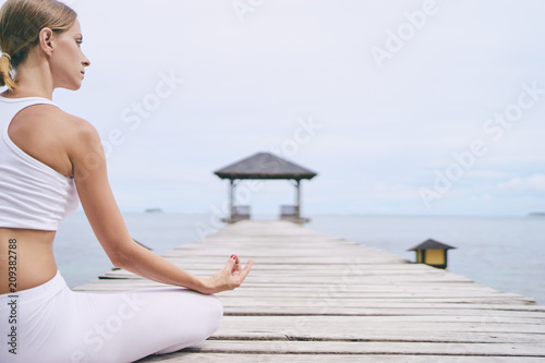 Yoga and meditation. Closeup of young woman in lotus pose on wooden deck with sea view.