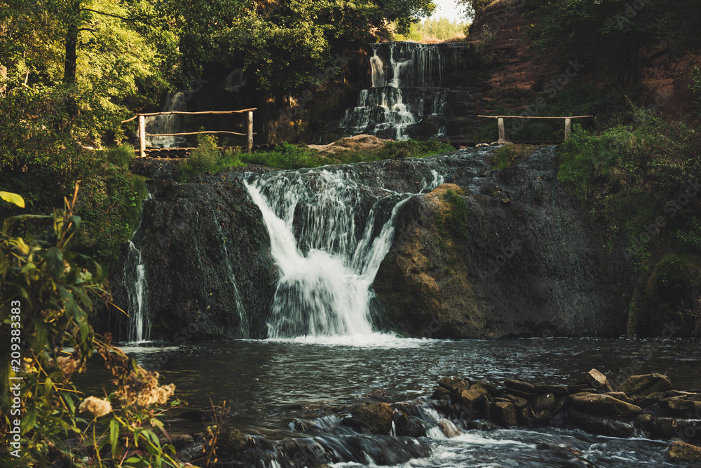 Obraz premium Beautiful mountain rainforest waterfall with fast flowing water and rocks, long exposure. Natural seasonal travel outdoor background in hipster vintage style
