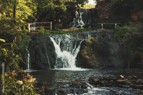 Beautiful mountain rainforest waterfall with fast flowing water and rocks  long exposure. Natural seasonal travel outdoor background in hipster vintage style