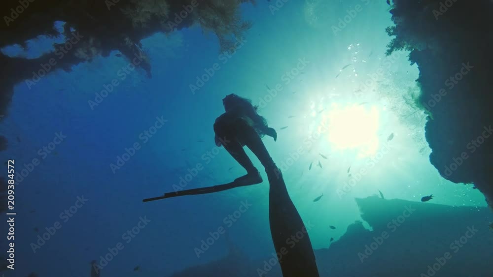 Freediver ascending to water surface from wreck in deep ocean