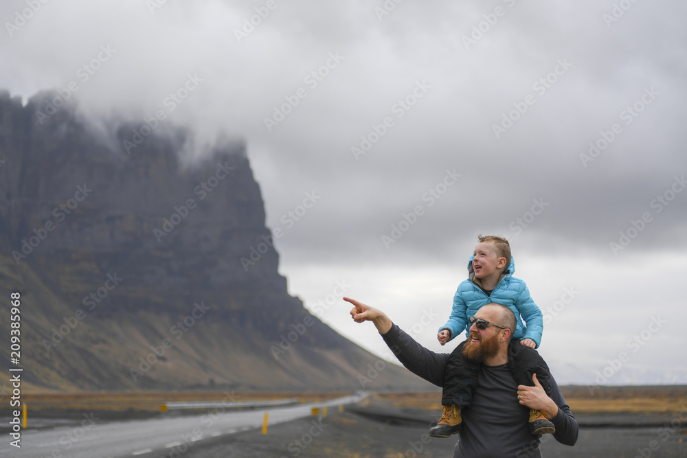 Dad points towards mountain as son on shoulders looks on Dad points towards mountain as son on shoulders looks on