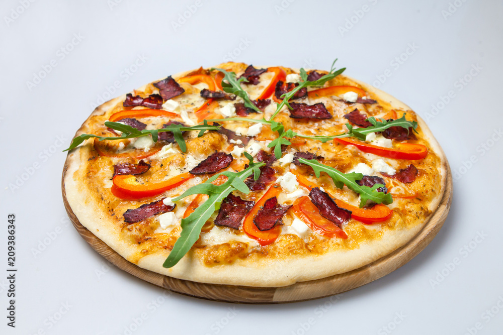 appetizing pizza with bacon, cheese and pepper is decorated with arugula lays on the board