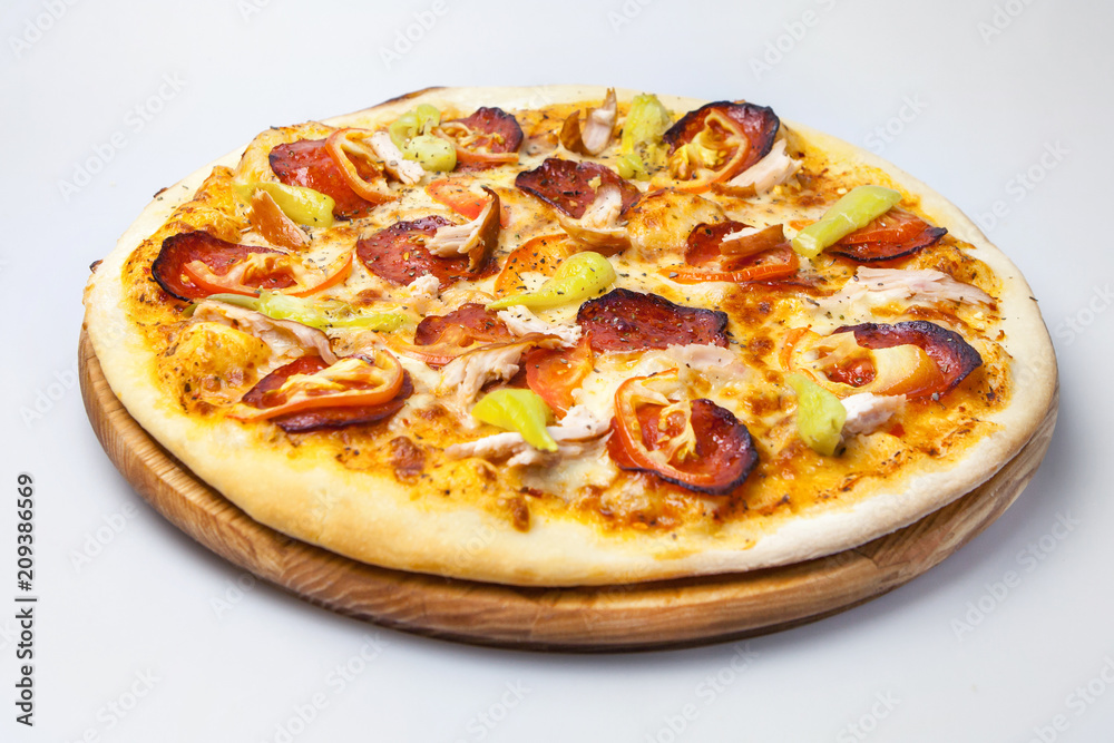 juicy cheese pizza with bits of bacon, with meat of chicken and with pepper is on a round board on a white background