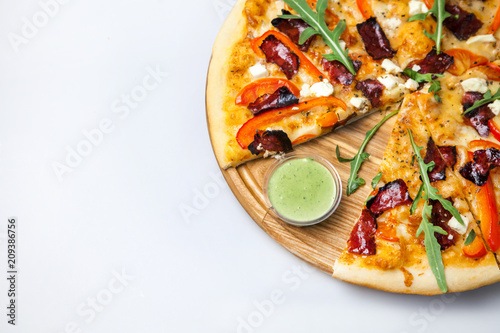 tasty sauce is on the board near pizza with baked bacon, with vegetables and cheese on a white background