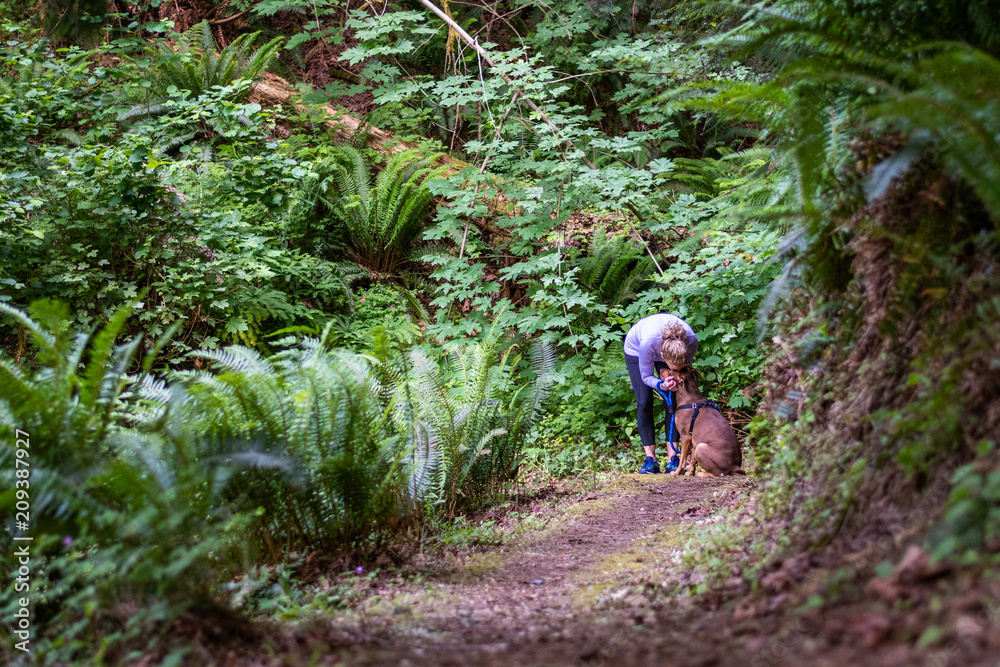 Female baby boomer in a purple top and black running pants in a quiet moment with her dog on a forest trail
