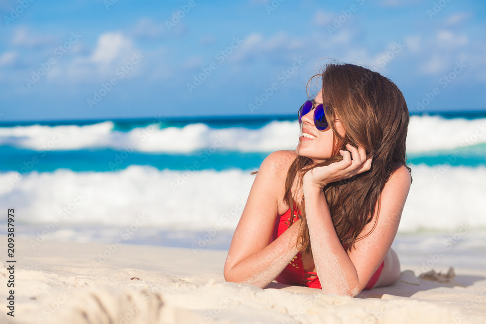 portrait of long haired woman in red swimsuit and sunglasses lying on tropical beach. La Digue, Seychelles