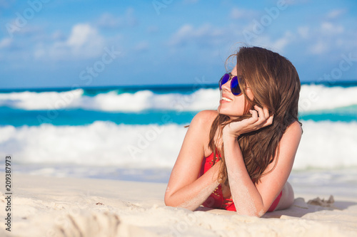 portrait of long haired woman in red swimsuit and sunglasses lying on tropical beach. La Digue, Seychelles