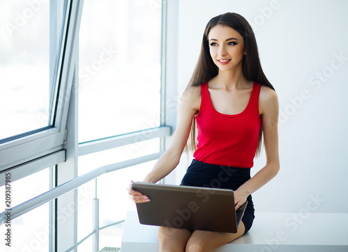 Business. Business Woman Dressed in Red T-Shirt and Black Skirt is Working on the Computer. Girl Sits on the Table and Smiles. High Resolution Free Download Business. Business Woman Dressed in Red T-Shirt and Black Skirt is Working on the Computer. Girl Sits on the Table and Smiles. High Resolution - GFXLoad