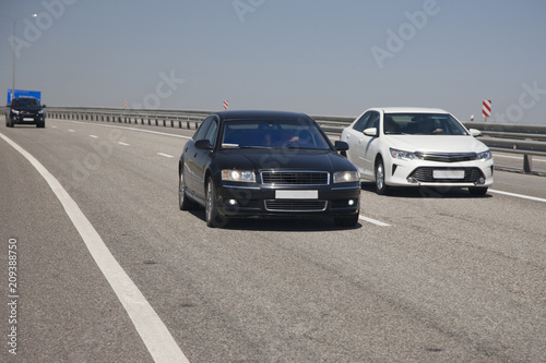 White and black sedans drive along the highway © biggur