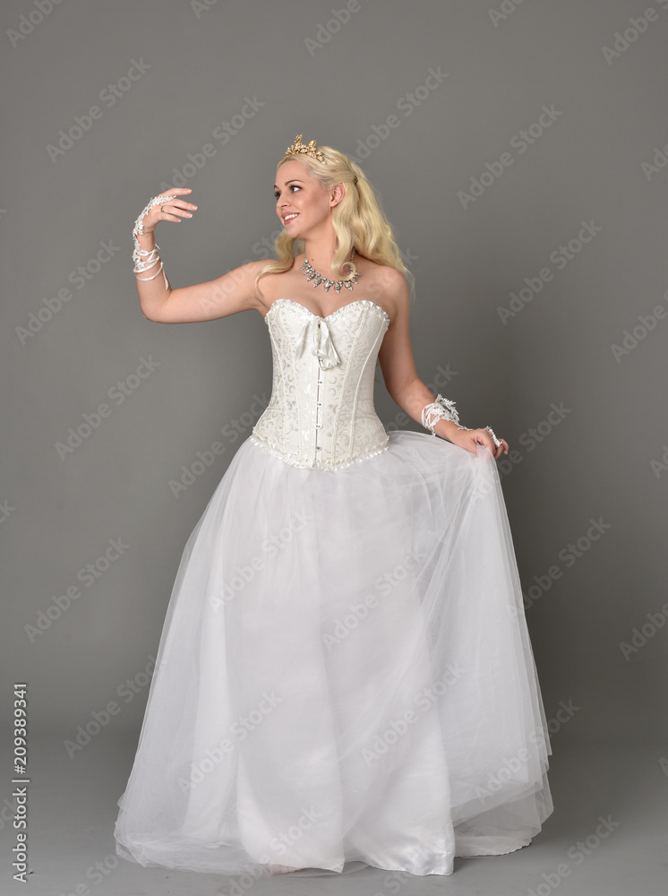 full length portrait of blonde girl wearing white corset gown. standing pose on grey studio background. full length portrait of blonde girl wearing white corset gown. standing pose on grey studio background.