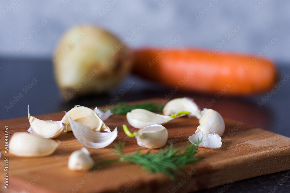 Garlic, onion, carrot and greens on a wooden board background and gray background in a soft background blur Garlic, onion, carrot and greens on a wooden board background and gray background in a soft background blur