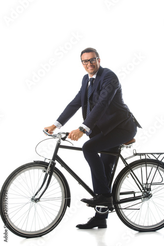 smiling businessman in eyeglasses sitting on bicycle isolated on white background