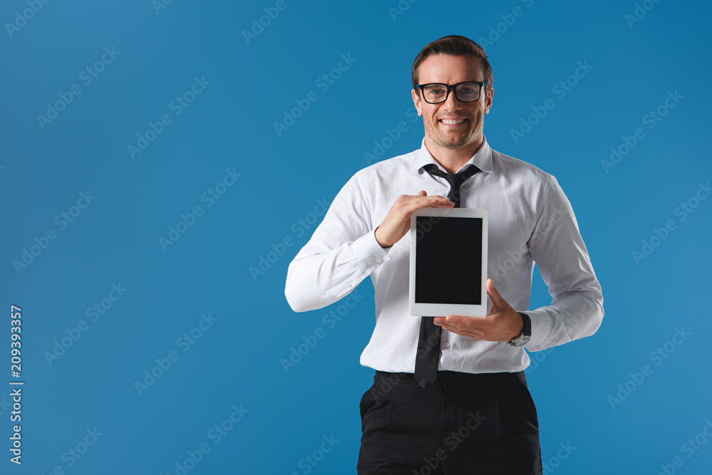 handsome man in eyeglasses holding digital tablet with blank screen and smiling at camera isolated on blue