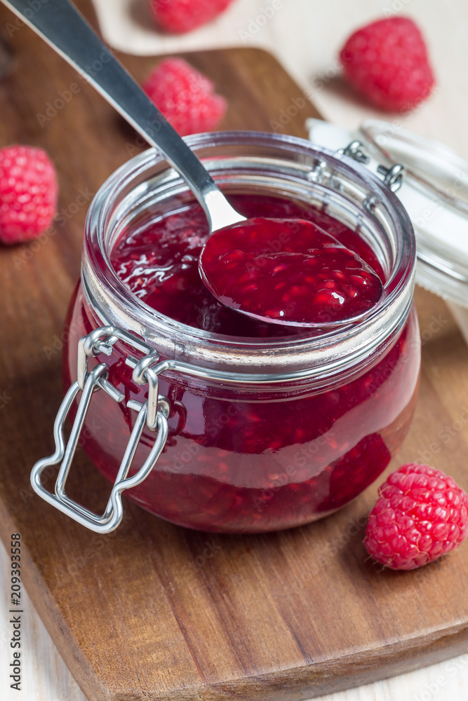 Raspberry jam in glass jar on a wooden board, vertical Raspberry jam in glass jar on a wooden board, vertical