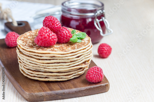 Stack of pancakes or fritters with raspberry on wooden board, raspberry jam on background, horizontal, copy space