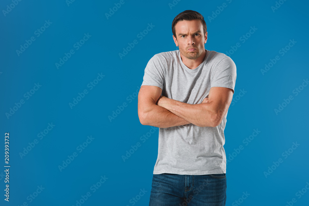 frowning man standing with crossed arms and looking at camera isolated on blue frowning man standing with crossed arms and looking at camera isolated on blue