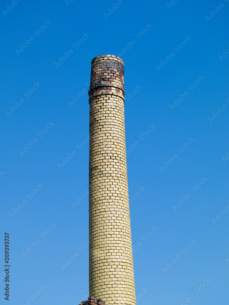 Altenburg / Germany: Yellow clinker chimney of an old shut down malt coffee factory in front of a deep blue sky