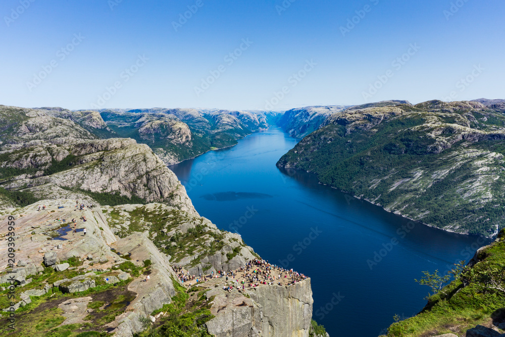 View at lysefjorden from above Preikestolen/Pulpit Rock in Norway with a clear blue sky. Lysefjorden, the Norwegian landscape and all the tourists standing at Preikestolen/Pulpit Rock.