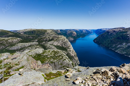 View at lysefjorden from above Preikestolen/Pulpit Rock in Norway with a clear blue sky. Lysefjorden, the Norwegian landscape and all the tourists standing at Preikestolen/Pulpit Rock.