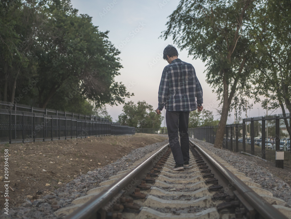 young alone man walking on the railroad track between the trees young alone man walking on the railroad track between the trees